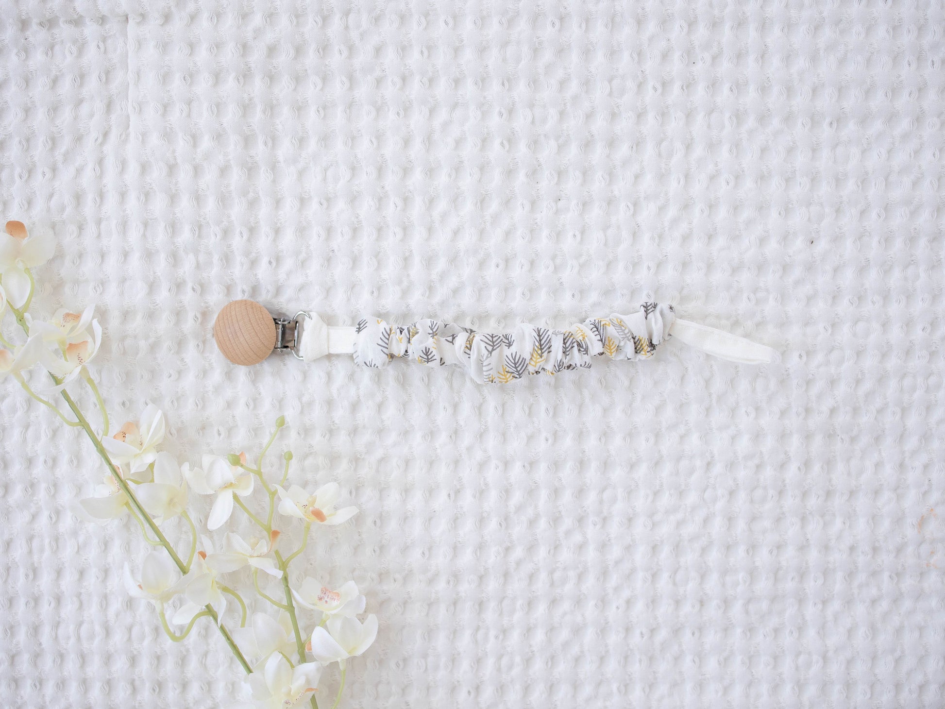Baby pacifier clip with floral design on a textured white background